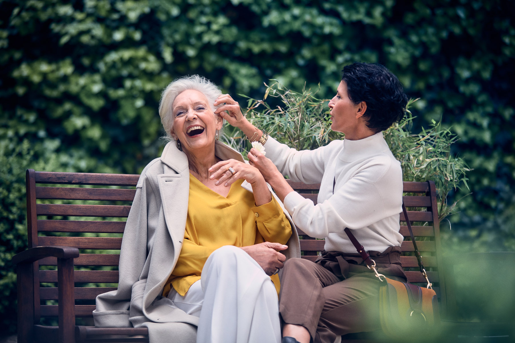 Zwei ältere Damen sitzen auf einer Parkbank und unterhalten sich lachend.