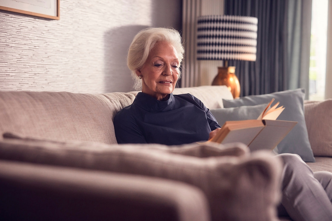 Eine ältere Dame lesend auf ihrer Couch