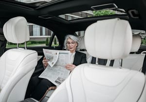 Frau liest auf Rückbank von KFZ Zeitung, sicher durch Begleitschutz von RAS Security Services