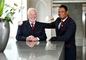 Junger und älterer Mitarbeiter von RAS Services stehen in Uniform hinter Empfangsdesk