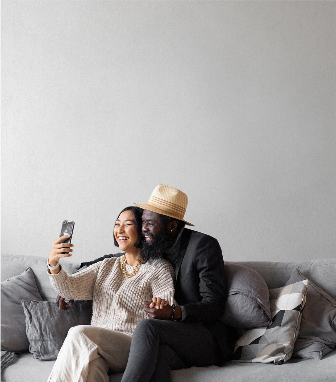 Mann und Frau sitzen auf grauem Sofa und nutzen RAS Concierge App auf dem Smartphone