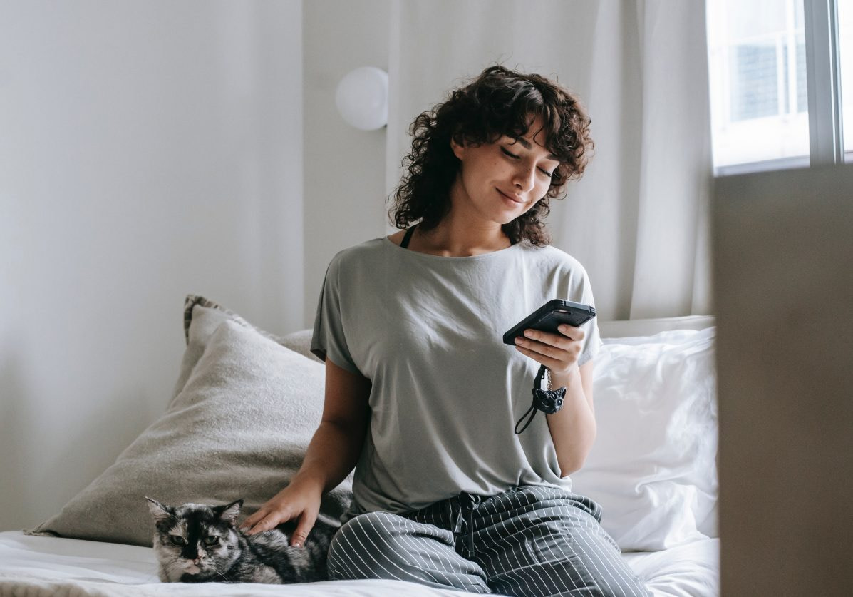 Frau sitzt auf Bett und blickt auf Handy - RAS Loyalty Concierge bietet eine einfache Concierge App