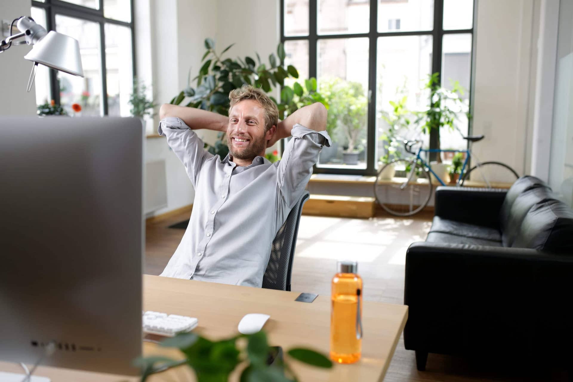 Online Händler, der den easyCredit-Ratenkauf einsetzt, sitzt entspannt am Schreibtisch und lehnt sich lächelnd zurück.