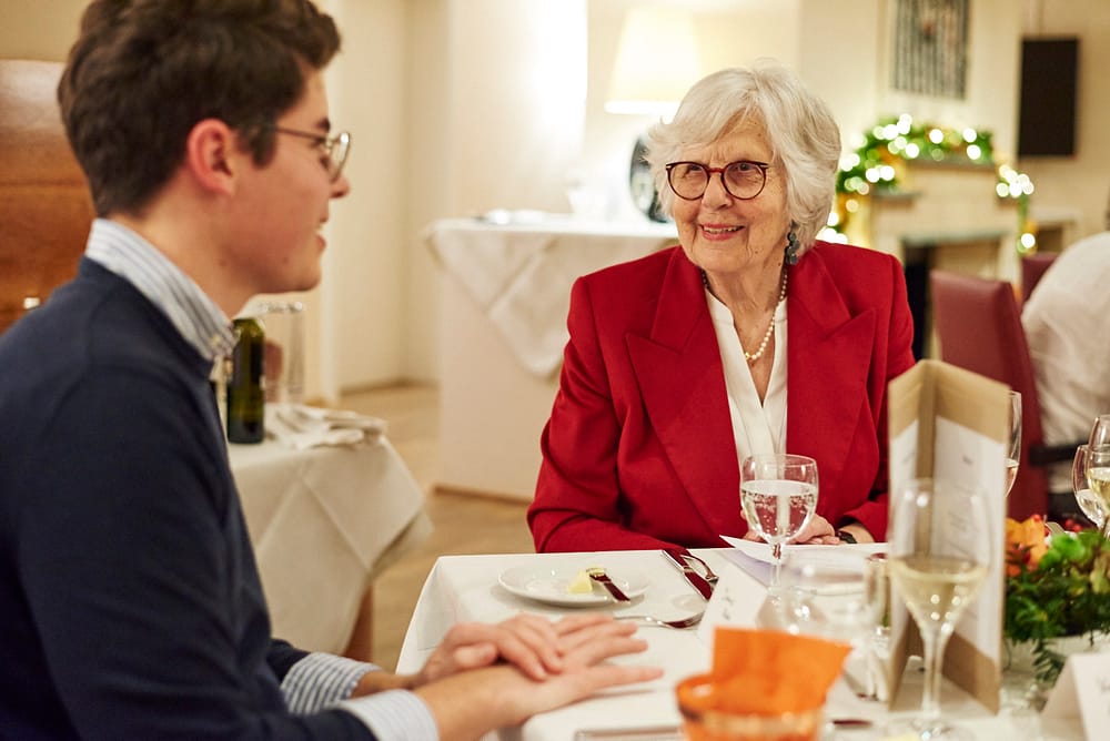 Seniorin in rotem Blazer spricht mit Student beim Tertianum Generationendinner