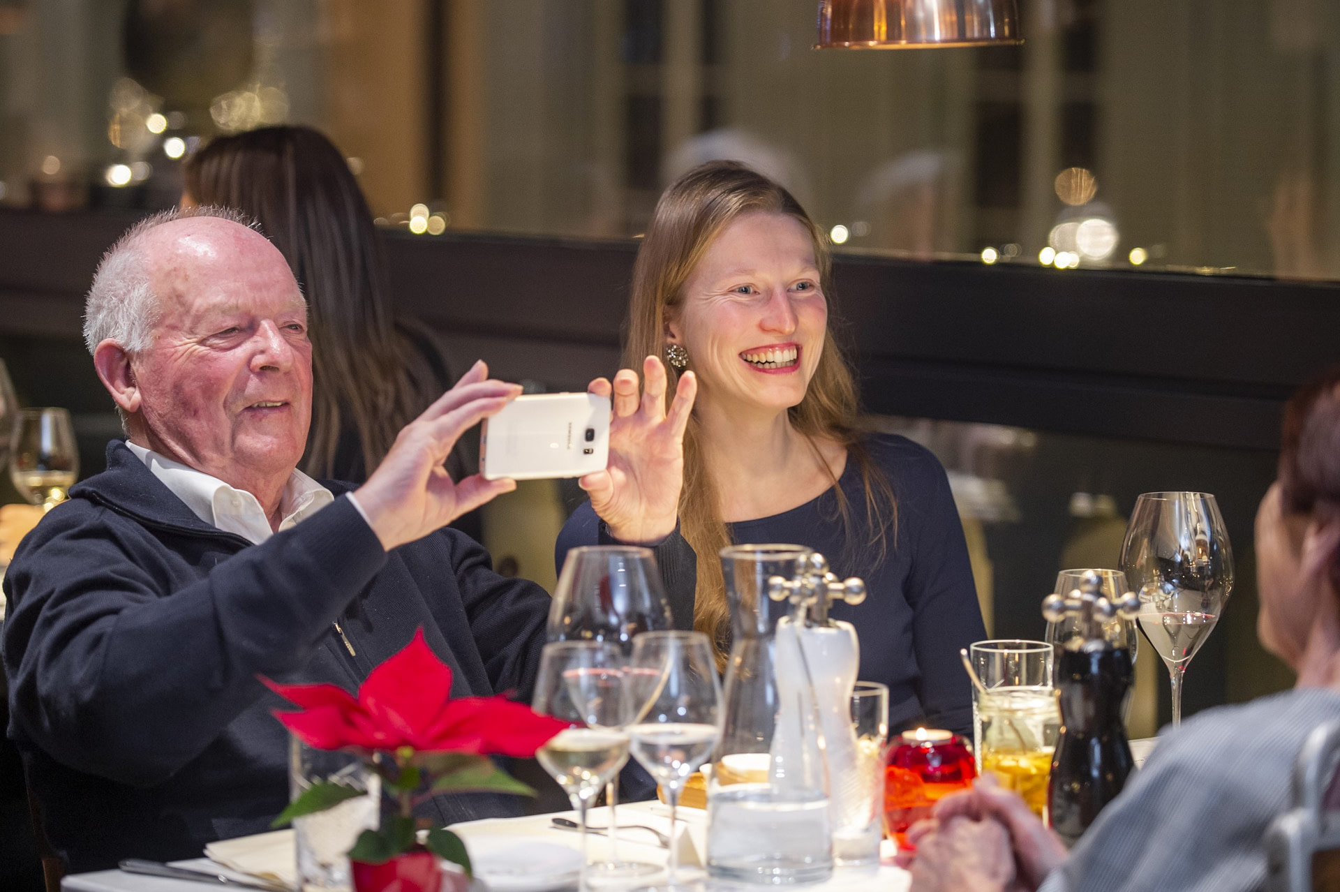 Glücklicher älterer Herr macht ein Handyfoto vom Gegenüber im Restaurant beim Mehrgenerationendinner
