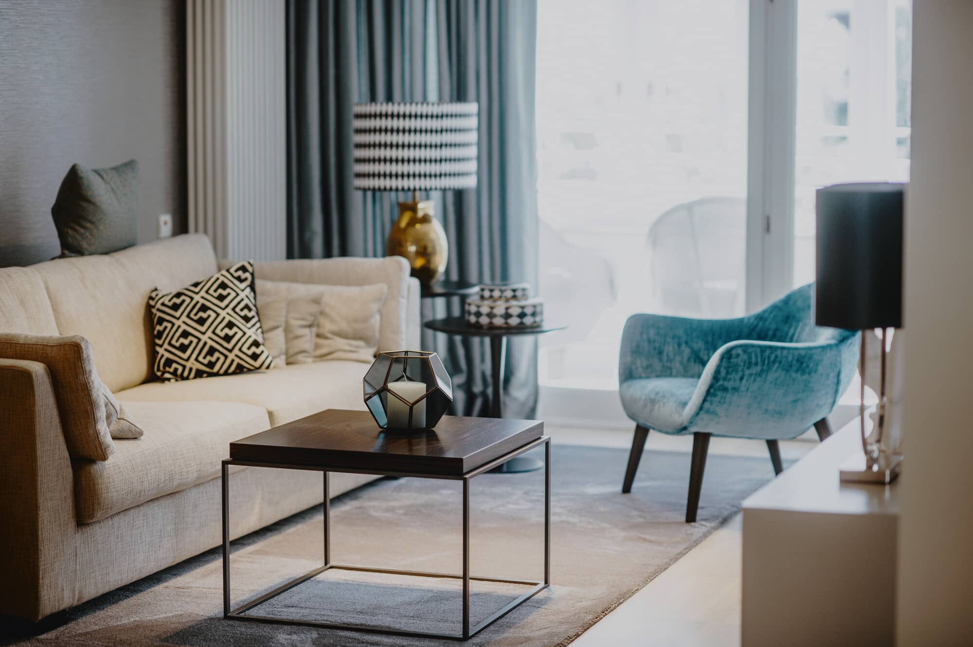 Das Wohnzimmer einer Gästewohnung mit Sessel, Sofa, Couchtisch und großem Fenster in der Tertianum Senioreneinrichtung.