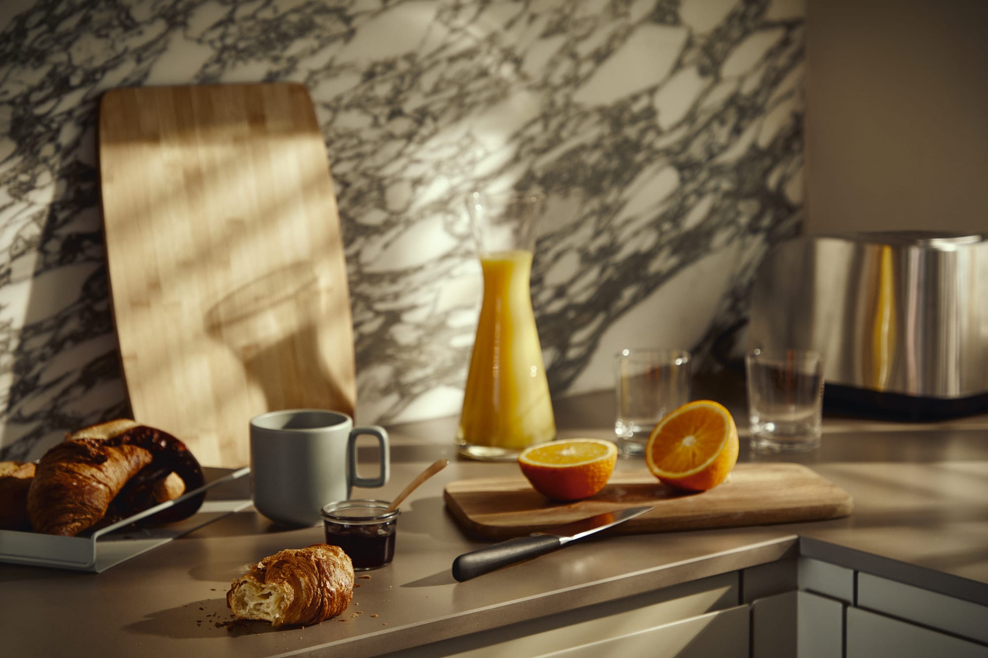 Küchenanrichte mit Schneidebrettern, einer aufgeschnittenen Orange, Orangensaft und Croissants