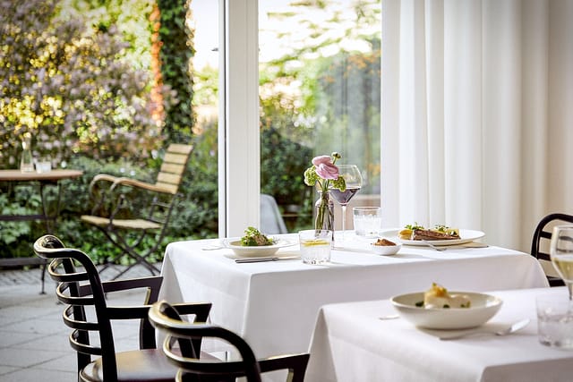 Ein weiß gedeckter Tisch mit gutem Essen und Blumen mit Blick in den grünen Garten in der Tertianum Senioreneinrichtung.