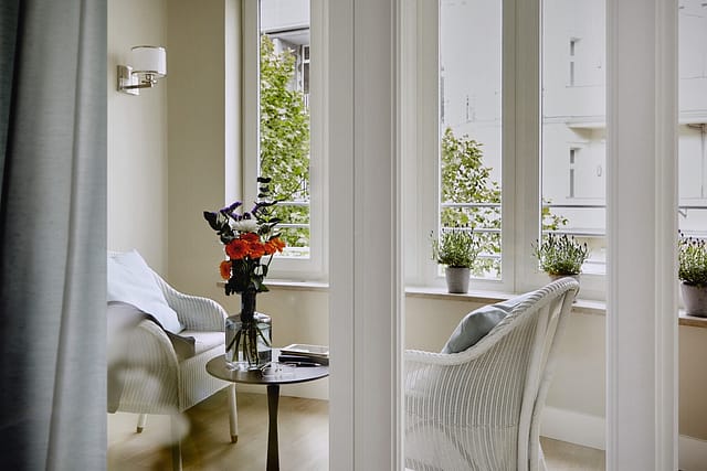 Ein lichtdurchfluteter Wintergarten mit gemütlichen, weißen Stühlen in einer Gästewohnung in der Tertianum Senioreneinrichtung.