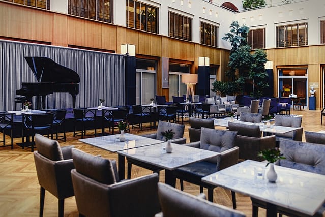 Verschiedene Sitzmöglichkeiten mit Tischen, Pflanzen und einem Piano im Atrium des Seniorenhaus Tertianum