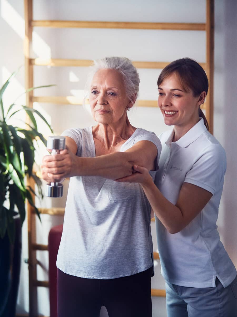 Eine Seniorin bei der Gymnastik mit einer Pflegerin