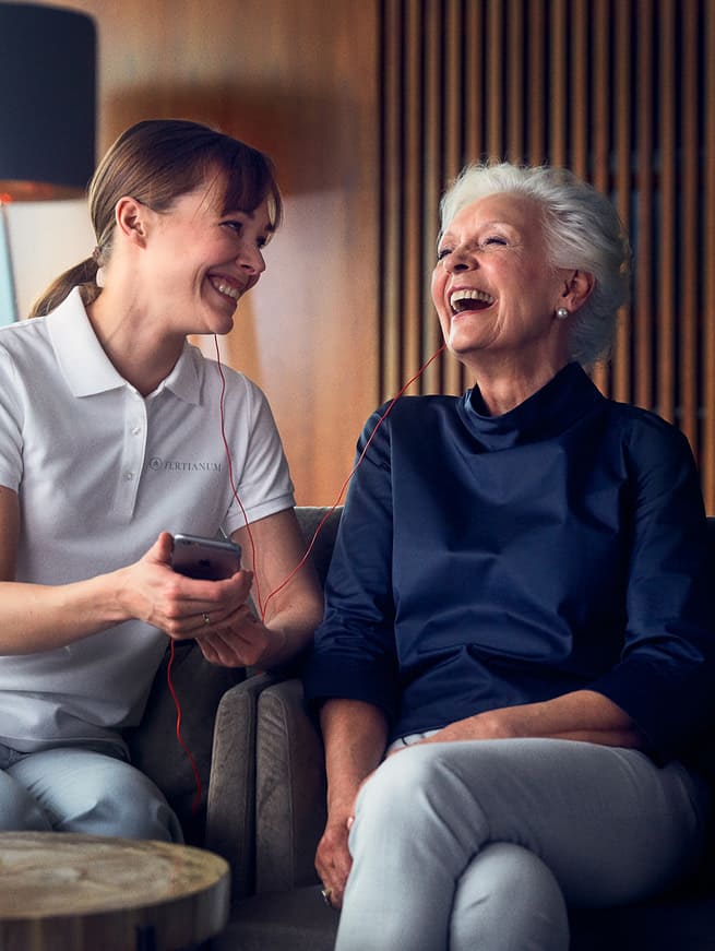 Eine lachende ältere Dame, die von einer Pflegerin betreut wird im Seniorenhaus Tertianum.