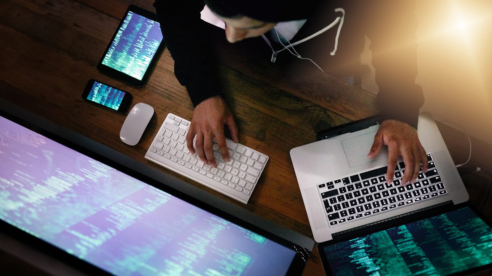 Symbolbild eines Hackers, der auf mehreren Tastaturen tippt und verschiedene Devices (PC, Laptop, Tablet & Smartphone) bedient.
