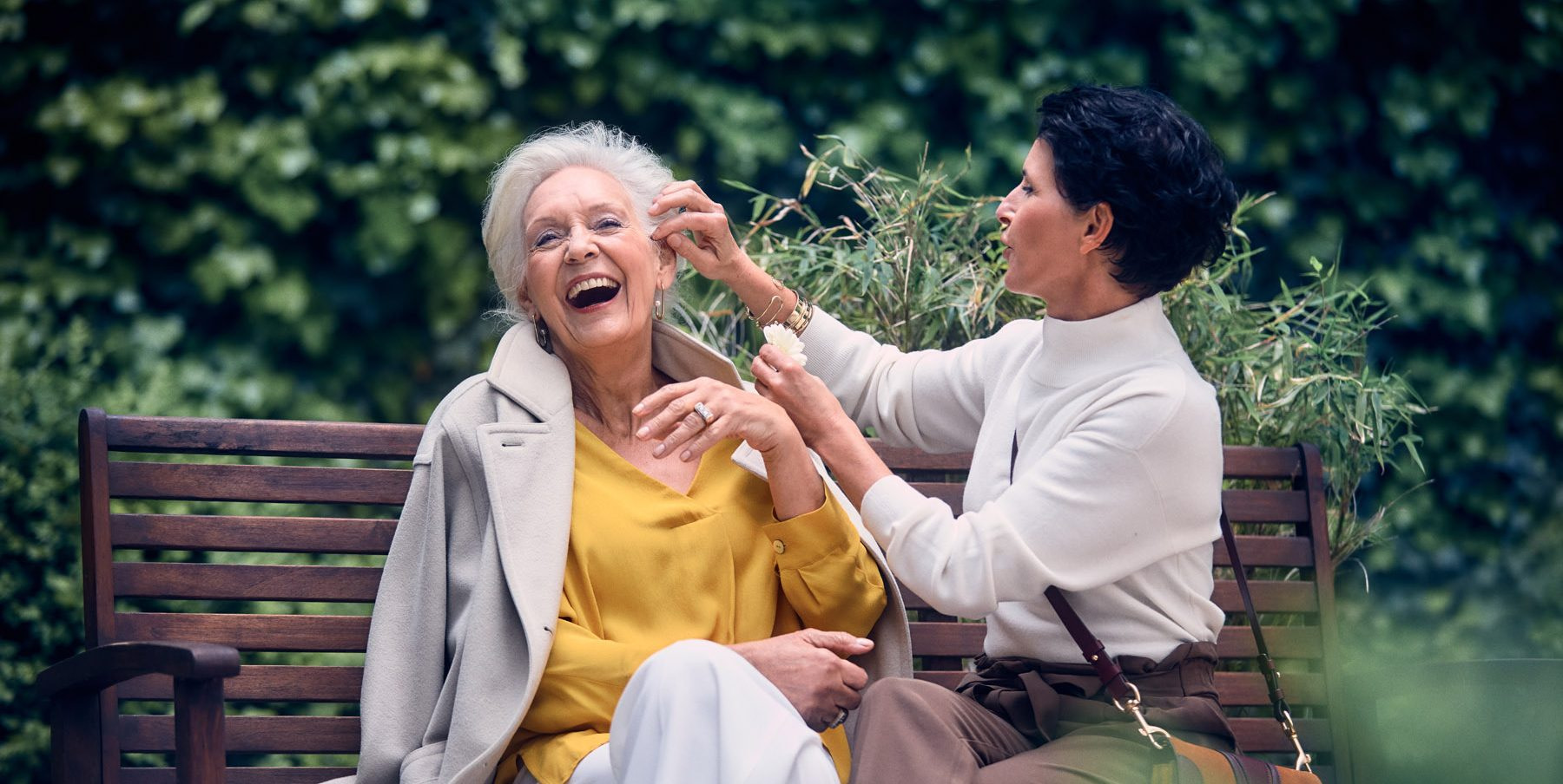 Lachende Seniorin mit Pflegehelferin im Garten der Tertianum Residenz.