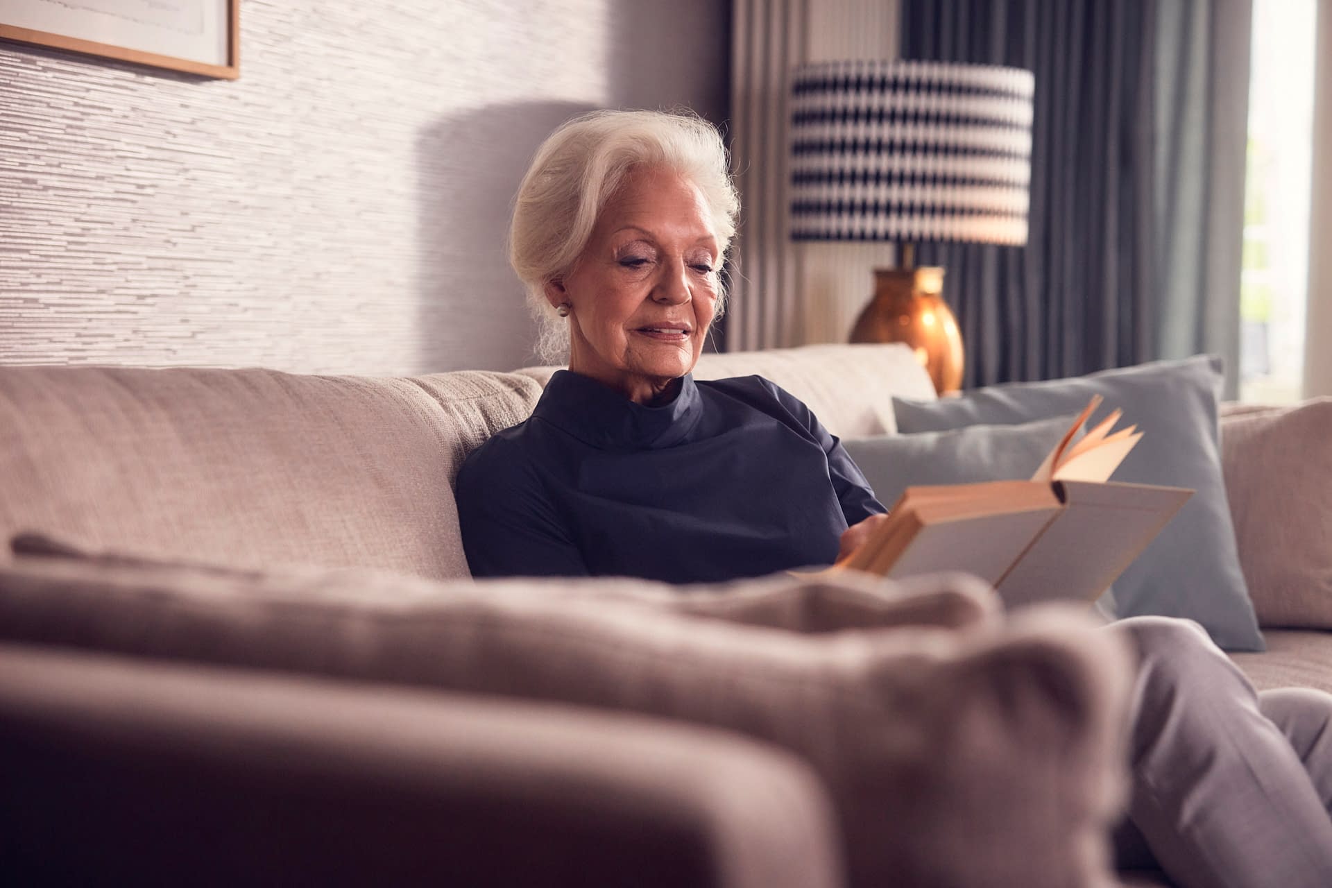 Eine ältere Dame beim Lesen in ihrer Seniorenwohnung