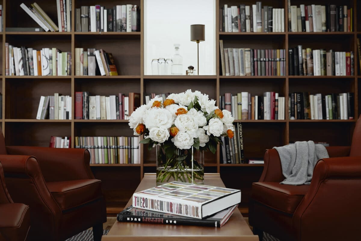 Eine Bibliothek mit Bücherregalen, zwei roten Sesseln und einem Blumenstrauß in der Tertianum Senioreneinrichtung.