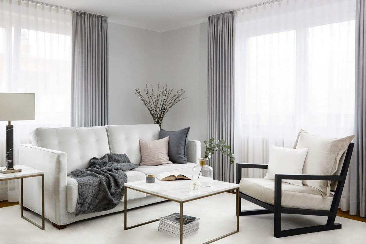 Eine weiße, gemütliche Couch, ein Sessel und ein Couchtisch in einem lichtdurchfluteten Wohnzimmer im Seniorenhaus Tertianum.