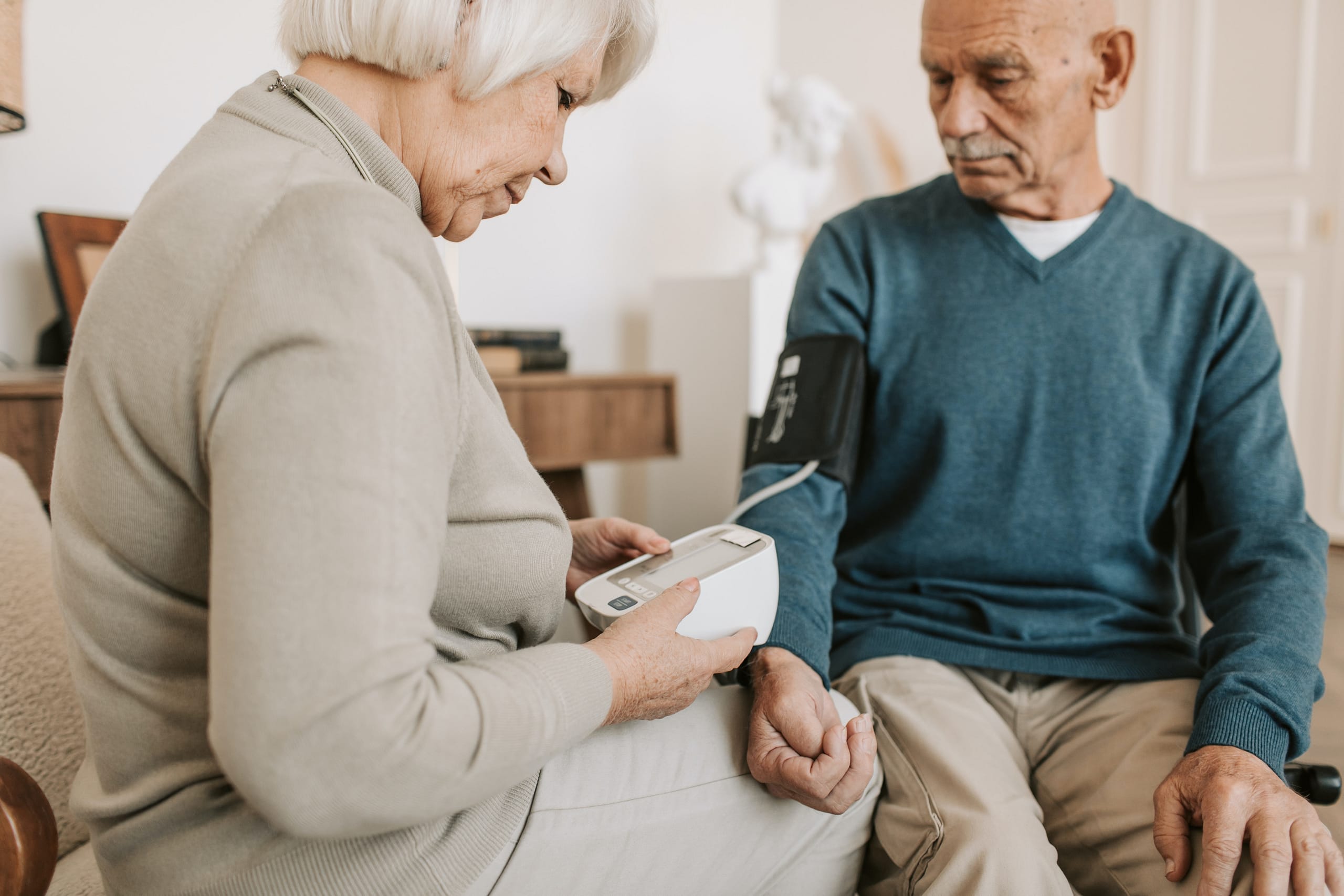 Eine Seniorin misst einem Senior mit einem Gerät den Blutdruck