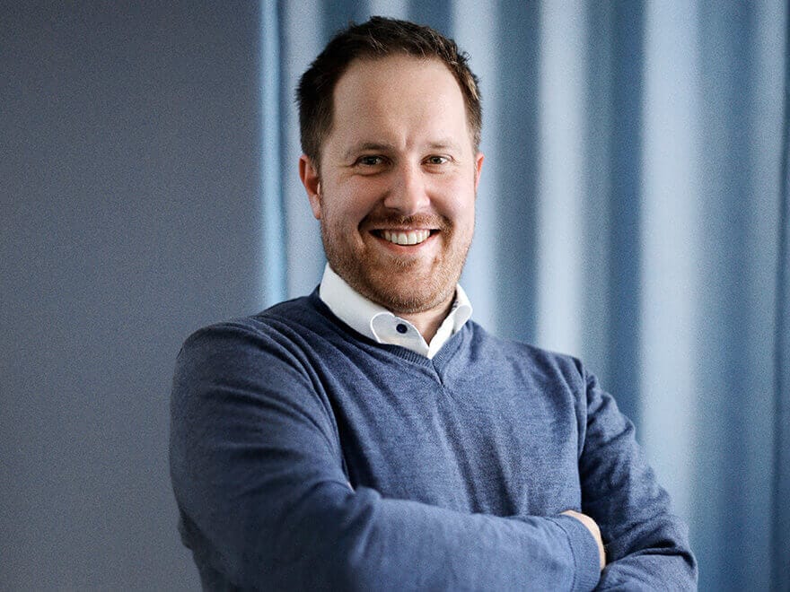 Portrait Bild von Manuel Mazoll mit braunen Haaren, blauem Pullover