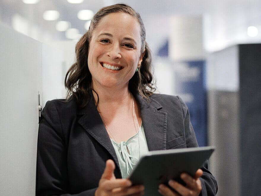 Portrait Bild von Michaela Schubert mit dunklen Haaren, schwarzem Blazer, hält ein Tablet